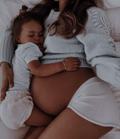 a pregnant woman is holding her baby while laying on the bed with it's stomach