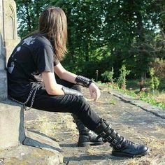 a man with long hair sitting on top of a cement pillar