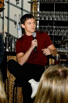 a man holding a microphone while sitting in front of a group of people at a bar