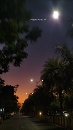 the night sky is lit up with street lights and palm trees on the side of the road