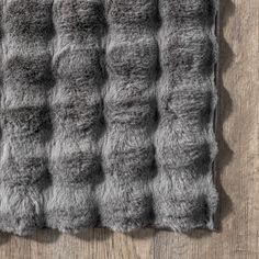 a gray rug on top of a wooden floor next to a white and black wall