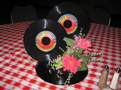 two black records sitting on top of a table next to pink flowers and silverware