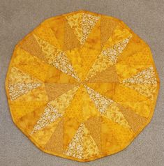 a yellow circular quilt on the floor with white and brown designs in it's center