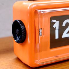 an orange alarm clock sitting on top of a wooden table