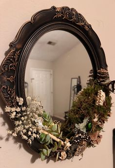 a mirror hanging on the wall with flowers and greenery in it's reflection