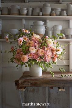 a vase filled with pink flowers sitting on top of a wooden table next to shelves