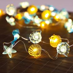 some lights that are sitting on top of a wooden table with shells and seashells around them