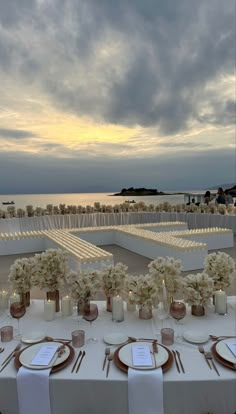 an outdoor wedding setup with white flowers and gold place settings on a table in front of the ocean