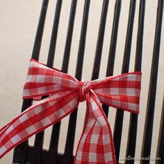 a red and white bow sitting on the back of a black chair with wood slats