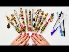 a woman's hands surrounded by various jewelry and pens on top of a white surface