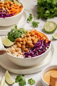 two white bowls filled with rice, carrots and lettuce next to dipping sauce