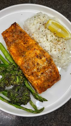 a white plate topped with fish, rice and asparagus next to broccoli