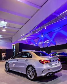 two cars are parked in a showroom with purple lighting on the ceiling and blue lights above them