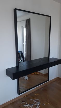 a mirror sitting on top of a wooden floor in front of a wall mounted shelf