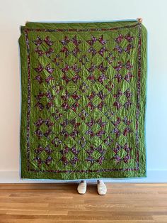 a green quilt with red and purple flowers on it sitting on top of a wooden floor