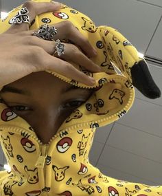 a person wearing a yellow pokemon hoodie with rings on their fingers and holding onto the hood