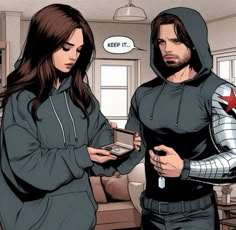 a man and woman dressed in hoodies looking at something on a tablet screen while standing next to each other