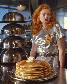 a woman standing in front of a stack of pancakes