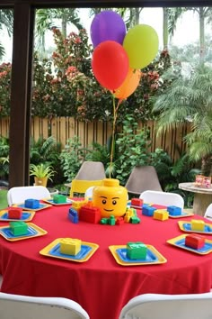 a red table topped with lots of balloons and legos next to a fenced in area