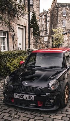 a small black car parked in front of a brick building on a cobblestone street