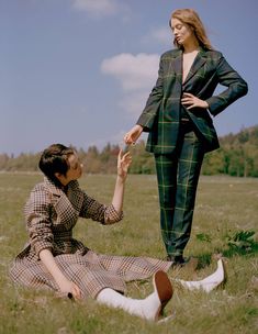 two women sitting in the grass with one holding her hand out to another woman's hand