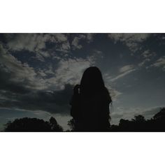 the silhouette of a woman with long hair against a cloudy sky, holding a cell phone up to her ear