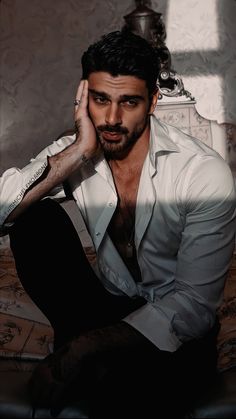 a man sitting on top of a bed wearing a white shirt and black pants with his hand under his head