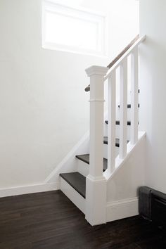 a white stair case next to a window in a room with hard wood flooring