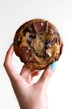 a hand holding a chocolate chip cookie with peanut butter on top and sea salt in the middle