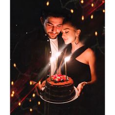 a man and woman standing next to each other in front of a cake with lit candles