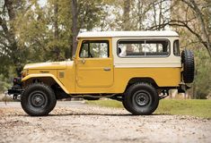 an old yellow jeep is parked on the side of the road in front of some trees