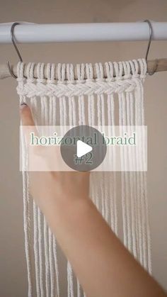 a hand is holding the end of a white macrame hanging from a metal rod