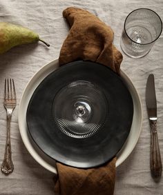 an empty plate and silverware on a white table cloth with a brown napkin next to it