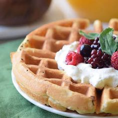 a white plate topped with waffles covered in whipped cream and berries next to a glass of orange juice