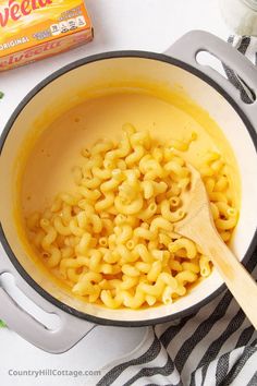 macaroni and cheese being cooked in a pot with a wooden spoon next to it