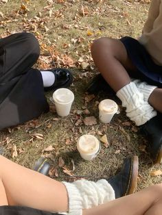 two people sitting on the ground with their legs crossed and holding coffee cups in front of them