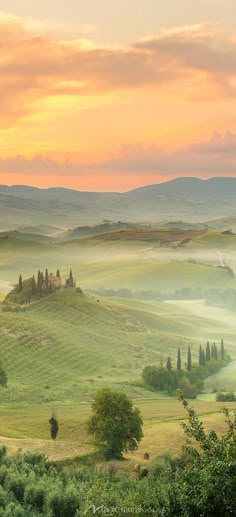 the rolling hills are covered in fog and clouds as the sun sets over the countryside