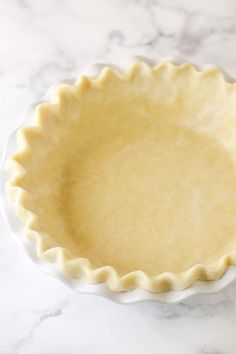 an uncooked pie crust in a white dish on a marble countertop with a red pepper