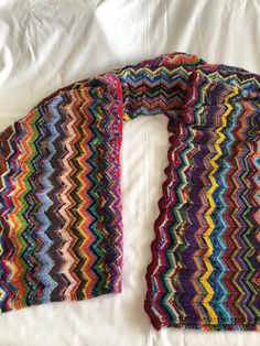 a multicolored knitted scarf laying on top of a white bed coverlet