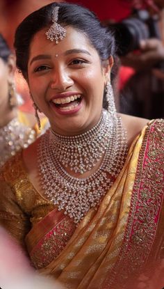 a woman in a gold sari smiles at the camera while wearing an elaborate necklace and earrings