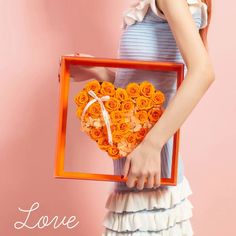 a woman holding a heart shaped box filled with orange roses