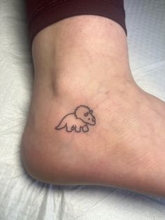 a small tattoo on the foot of a person with a dinosaur drawn on it's side