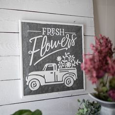 a sign that says fresh flowers on the side of a white wall next to potted plants