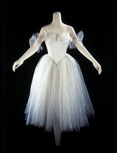 a white ballerina dress on display in front of a black background with an angel wing