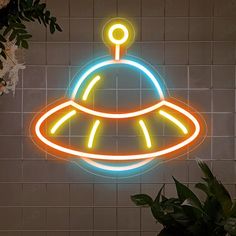 a neon sign on the wall above a potted plant in front of a tiled wall