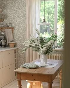 a vase with white flowers sitting on top of a wooden table next to a window