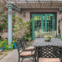 an outdoor dining table and chairs in front of a house with green doors on the side