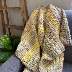 a crocheted blanket sitting on top of a gray couch next to a green plant