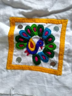 a white shirt with a colorful embroidered peacock on it's chest and yellow border