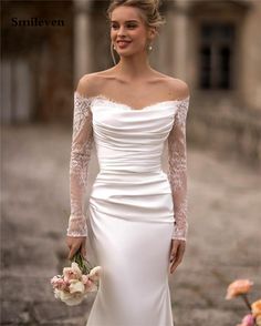 a woman in a white wedding dress holding flowers and smiling at the camera with her hands on her hips